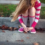Sad girl in striped shirt sitting on a curb.