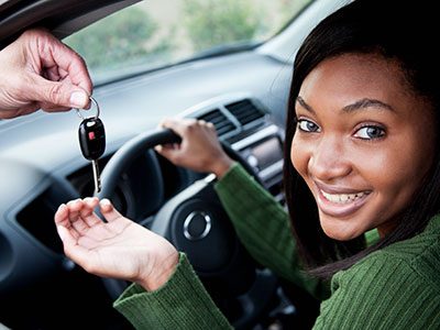 Teen girl sitting in car being handed the keys.
