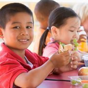 boy eating sandwich at school with other kids