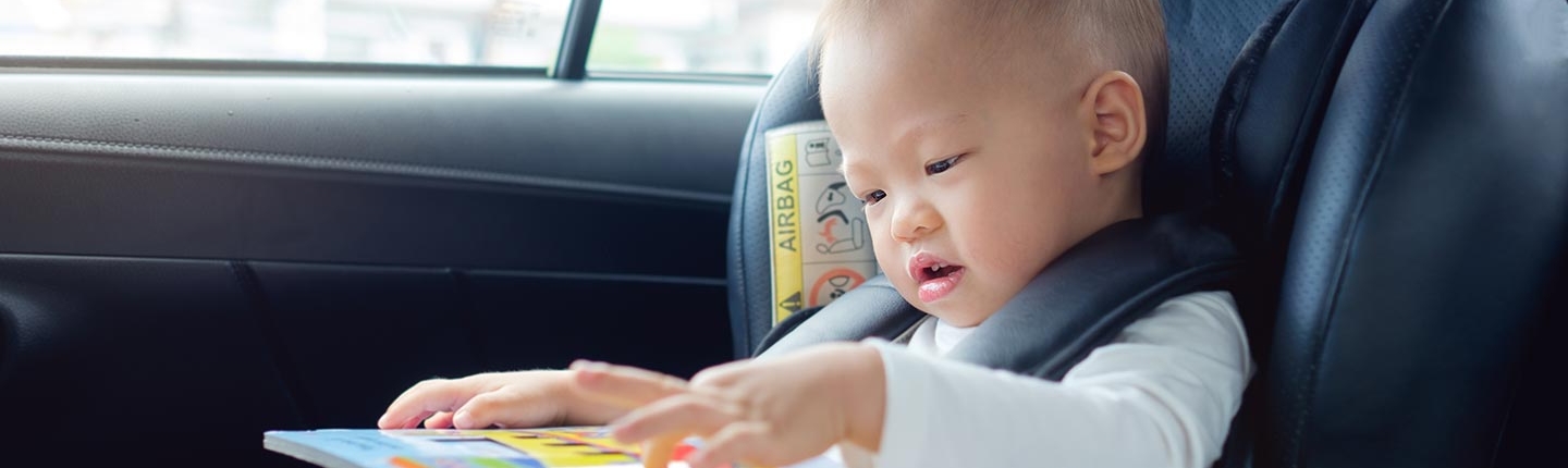 toddler boy sitting in car seat reading book