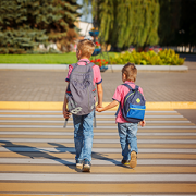 Two boys with backpack walking, holding on warm day on the road