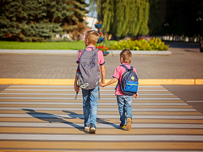 Two boys with backpack walking, holding on warm day on the road