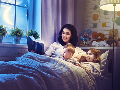 mom reading book to son and daughter in bed