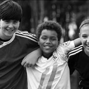 three kids in sports uniforms smiling