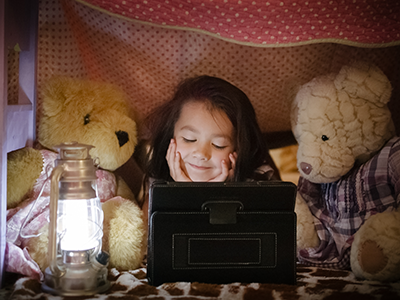 Little girl using tablet computer/tablet with teddy bears in fort