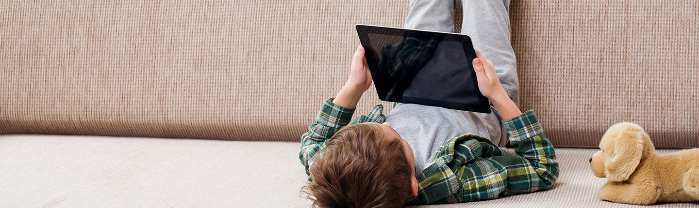 boy lying on couch using tablet