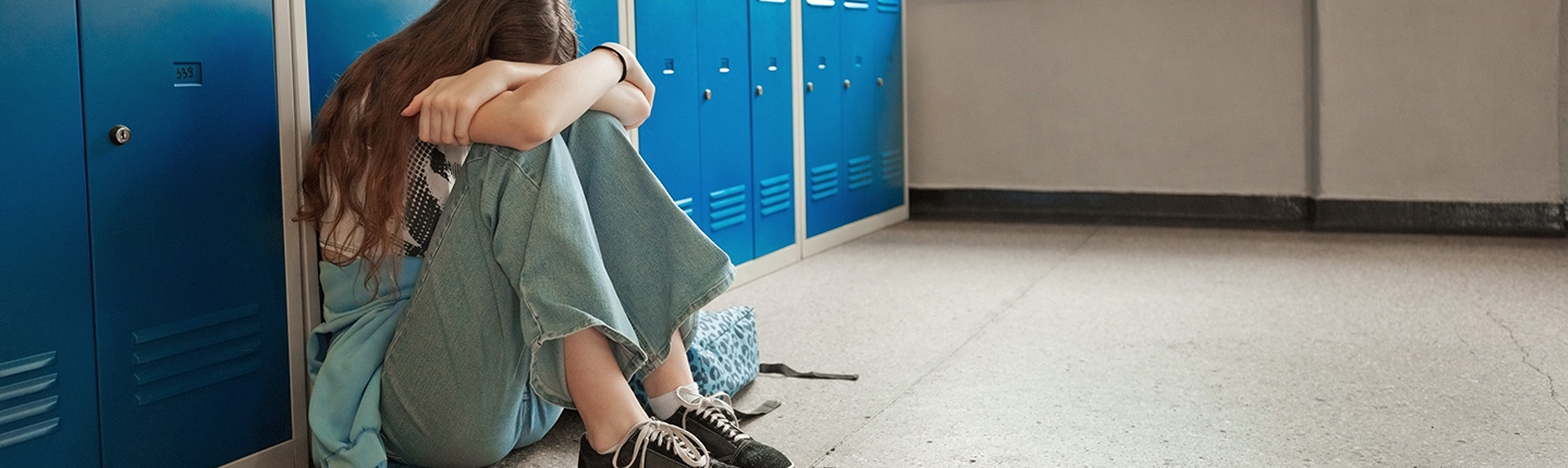 Girl sitting in the school hallway against the lockers with her head on her knees